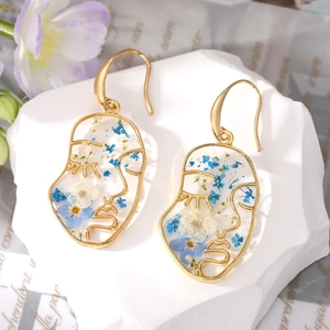Detailed view of gold face silhouette earrings with real blue and white dried flowers