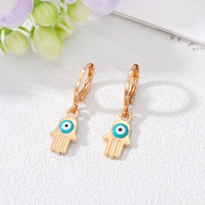 Detail of golden Hamsa Hand hoop earrings featuring Evil Eye charms on white stone surface