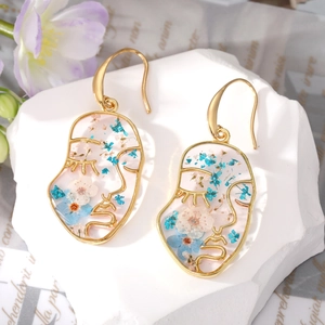 Artistic gold face earrings with blue dried flowers and resin inside geometric outlines