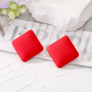 Close-up of red square stud earrings with matte texture on a white decorative pedestal