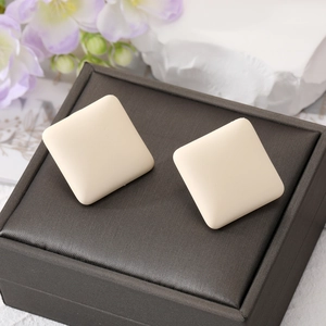 Macro detail of creamy white matte square stud earrings on a grey jewelry box cover