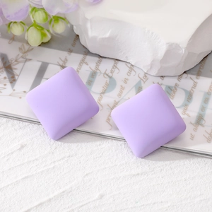 Close-up of matte lilac square stud earrings on a textured stone with purple flowers