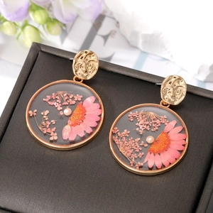 Elegante goldene runde Ohrringe mit rosa Trockenblumen und Perlen auf einer Schmuckbox