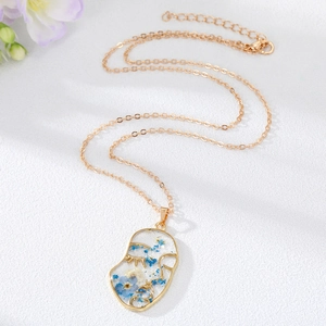 Detail view of abstract face pendant with real blue and white dried flowers in resin