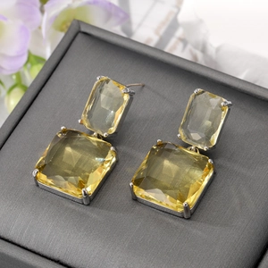 Elegant silver square earrings featuring yellow faceted crystal stones on a gray box