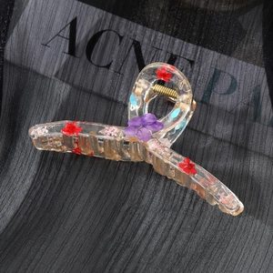 Elegant transparent resin hair claw with dried flowers on a black textured background