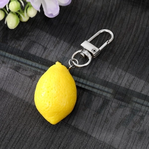 Realistic yellow lemon keychain with peel texture and silver lobster clasp on black fabric