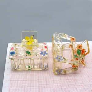 Detail view of rectangular hair claw clips with colorful dried flowers and green leaves