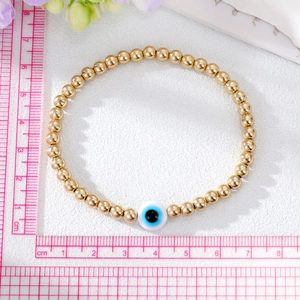 Bohemian gold beaded bracelet with blue evil eye charm on white textured background