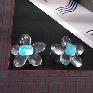 Primer plano de pendientes de flores de resina con cristal azul y escala de referencia