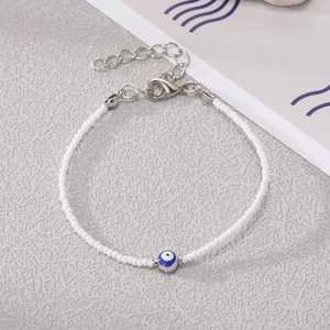 Close-up of bohemian white seed bead bracelet featuring a blue evil eye bead and silver clasp