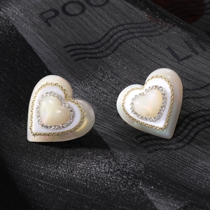Gros plan de boucles d'oreilles cœur en perle avec halo de strass et bord doré