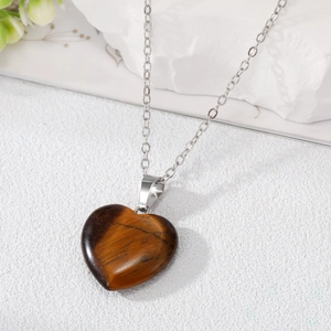 Macro shot of tiger eye stone heart pendant with polished silver chain on white stones
