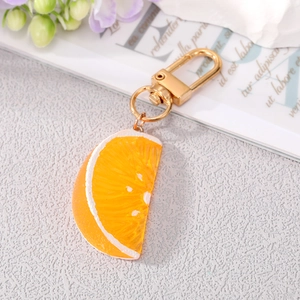 Detail view of a realistic orange slice keychain with golden lobster clasp on a flat lay