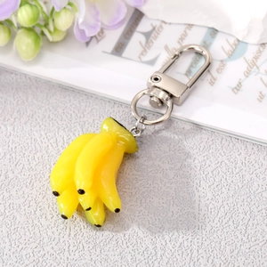 Realistic yellow banana cluster keychain with silver metal clip on a textured grey surface