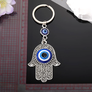 Silver Hamsa Hand keychain with Evil Eye bead on a reflective surface with a ruler