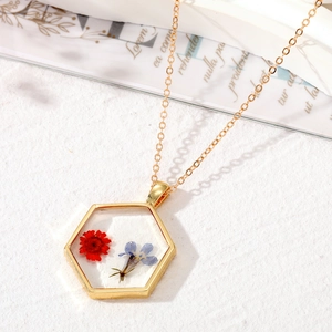 Vue macro du pendentif hexagonal en résine avec fleurs séchées et chaîne dorée
