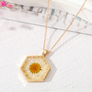 Détail macro du pendentif hexagonal doré avec une véritable marguerite blanche séchée