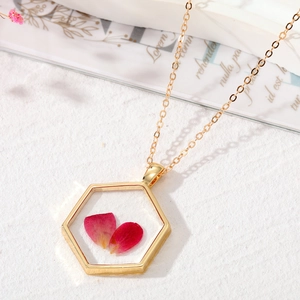 Détail macro du pendentif hexagonal doré avec de vraies fleurs séchées roses et chaîne