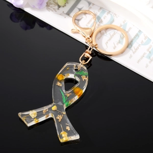 Bow-shaped resin keychain with yellow dried flowers and gold leaf on black surface
