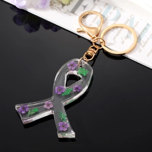 Floral resin bow keychain with dried flowers and gold clasp on a reflective surface