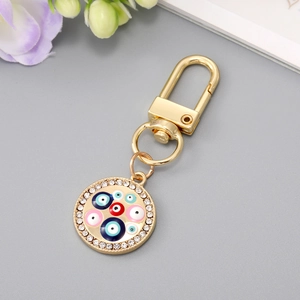 Golden heart-shaped devil eye keychain with sparkling rhinestones on grey background