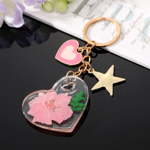 Détail d'un porte-clés en acrylique en forme de cœur avec fleur séchée rose et breloques dorées
