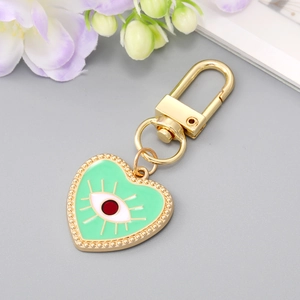 Close-up of a heart-shaped evil eye keychain with mint green enamel and gold finish