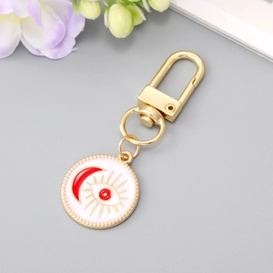 Detail of a golden evil eye keychain with white enamel and red crescent moon motifs