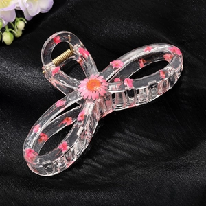 Close-up of large transparent resin hair claw clip with embedded pink dried flowers and daisy