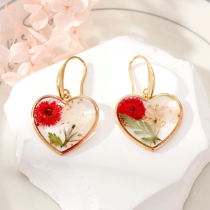 Detailed close-up of heart resin earrings with dried red and white flowers and gold foil