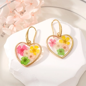 Detailed macro view of heart-shaped gold earrings with colorful pressed dried flowers