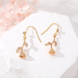 Detailed view of golden rose earrings with zircons on a white stone pedestal