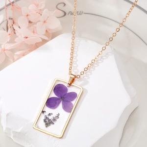 Gros plan d'un pendentif rectangulaire en résine avec fleurs séchées sur chaîne dorée