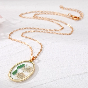Oval gold necklace with real white dried flowers and green leaves in resin pendant