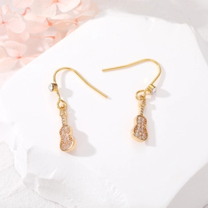 Close-up of golden guitar-shaped drop earrings with clear zircons on a white stone background