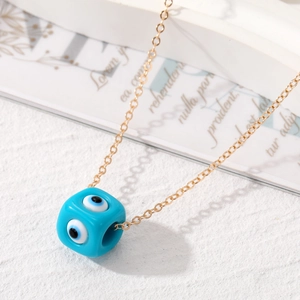 Nahaufnahme der goldenen Kette mit blauem Würfelanhänger und Evil-Eye-Details