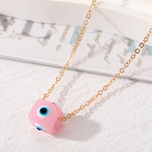 Makroaufnahme eines rosa Evil Eye Würfelanhängers mit goldener Kette auf weißem Grund