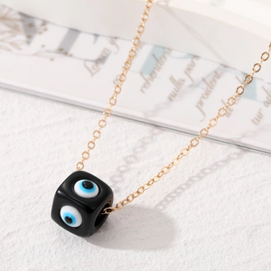 Nahaufnahme eines Harz-Evil-Eye-Würfels am Goldkettchen mit kunstvoller Karte im Bild