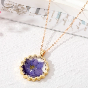 Collier bohème doré avec une fleur séchée violette dans un pendentif en résine ondulé