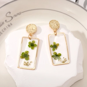 Detailed close-up of rectangular resin earrings with embedded green dried flowers