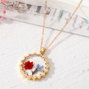 Gros plan d'un pendentif en résine dorée avec de véritables fleurs séchées rouges et bleues