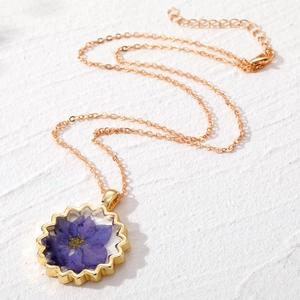 Collier bohème doré avec pendentif de fleur séchée violette sur surface texturée blanche