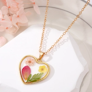 Détail macro du pendentif en cœur en résine avec de vraies fleurs séchées et chaîne dorée