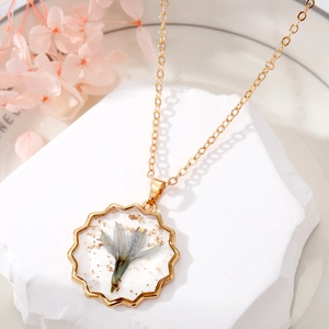 Gros plan du pendentif en résine dorée avec fleur séchée bleue et feuille d'or sur pierre