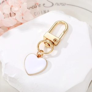 Close-up of heart-shaped white enamel keychain with gold metal lobster clasp on stone