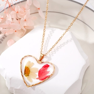 Vue macro d'un pendentif cœur doré avec de vraies fleurs séchées en résine sur pierre