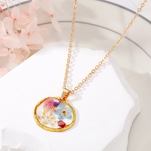 Détail d'un collier bohème doré avec un pendentif en résine aux fleurs séchées réelles
