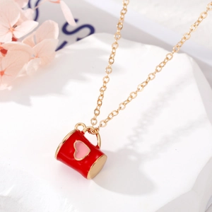 Détail macro du collier doré avec pendentif mug émaillé rouge et cœur sur marbre blanc