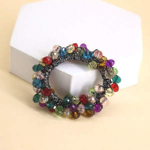 Détail de perles de cristal colorées sur des chouchous noirs posés sur un socle blanc